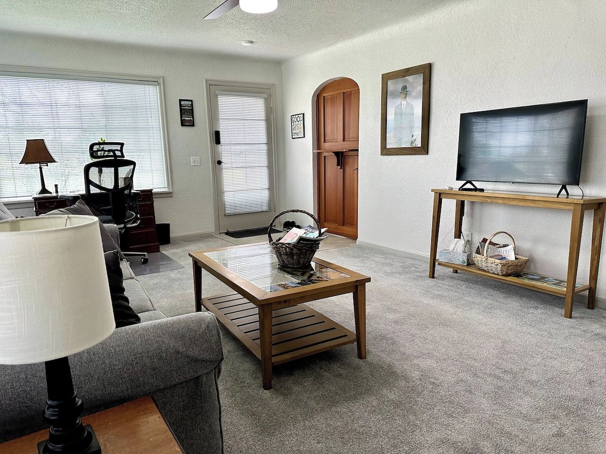 A living room with a sofa, a coffee table, a television on a stand, a lamp, and a door with a window.