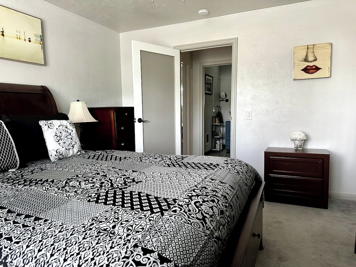 A bedroom with a patterned bedspread, a bedside table with a lamp, and a dresser.