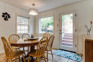 A dining area with a round wooden table and six chairs, a chandelier, and a door leading outside. - Stylish House w/ Backyard & Free Parking (Eugene)