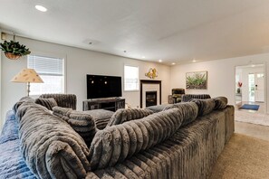A living room with a large sectional sofa, a flat-screen TV, a fireplace, and a hanging plant. - Stylish House w/ Backyard & Free Parking (Eugene)