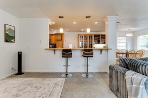 A modern kitchen with two bar stools, a dining area with a sofa, and a view of the kitchen through an open doorway. - Stylish House w/ Backyard & Free Parking (Eugene)