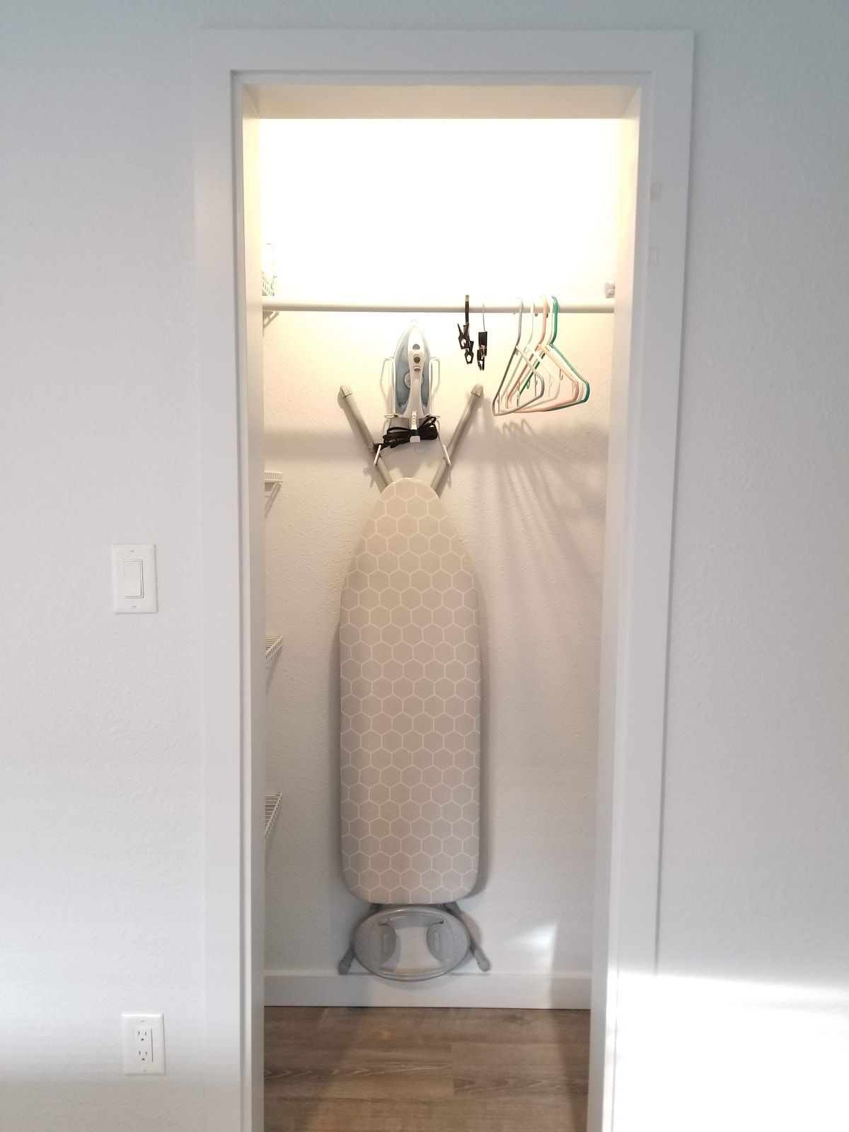 Quarto compacto com central de passar roupa embutida, cabideiro e tomada na parede.