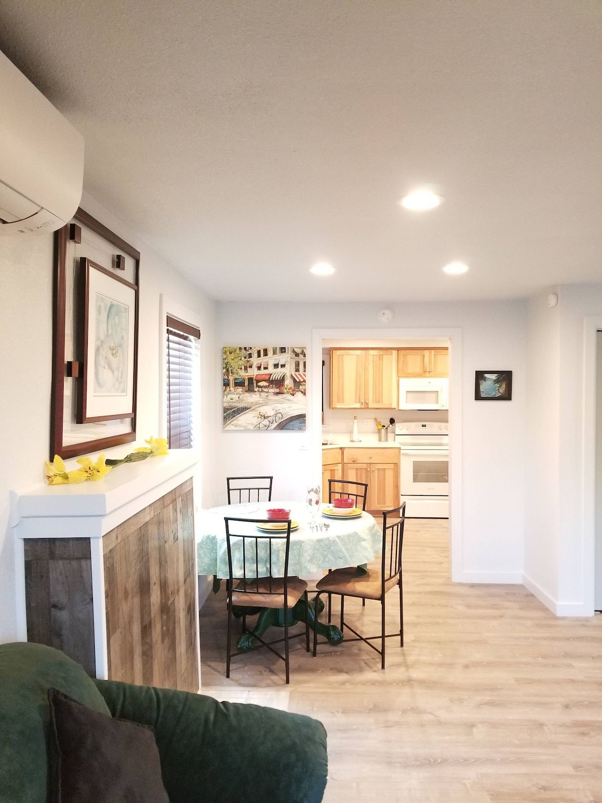 Uma sala de jantar com mesa posta para dois, cozinha ao fundo e sala de estar com sofá verde.
