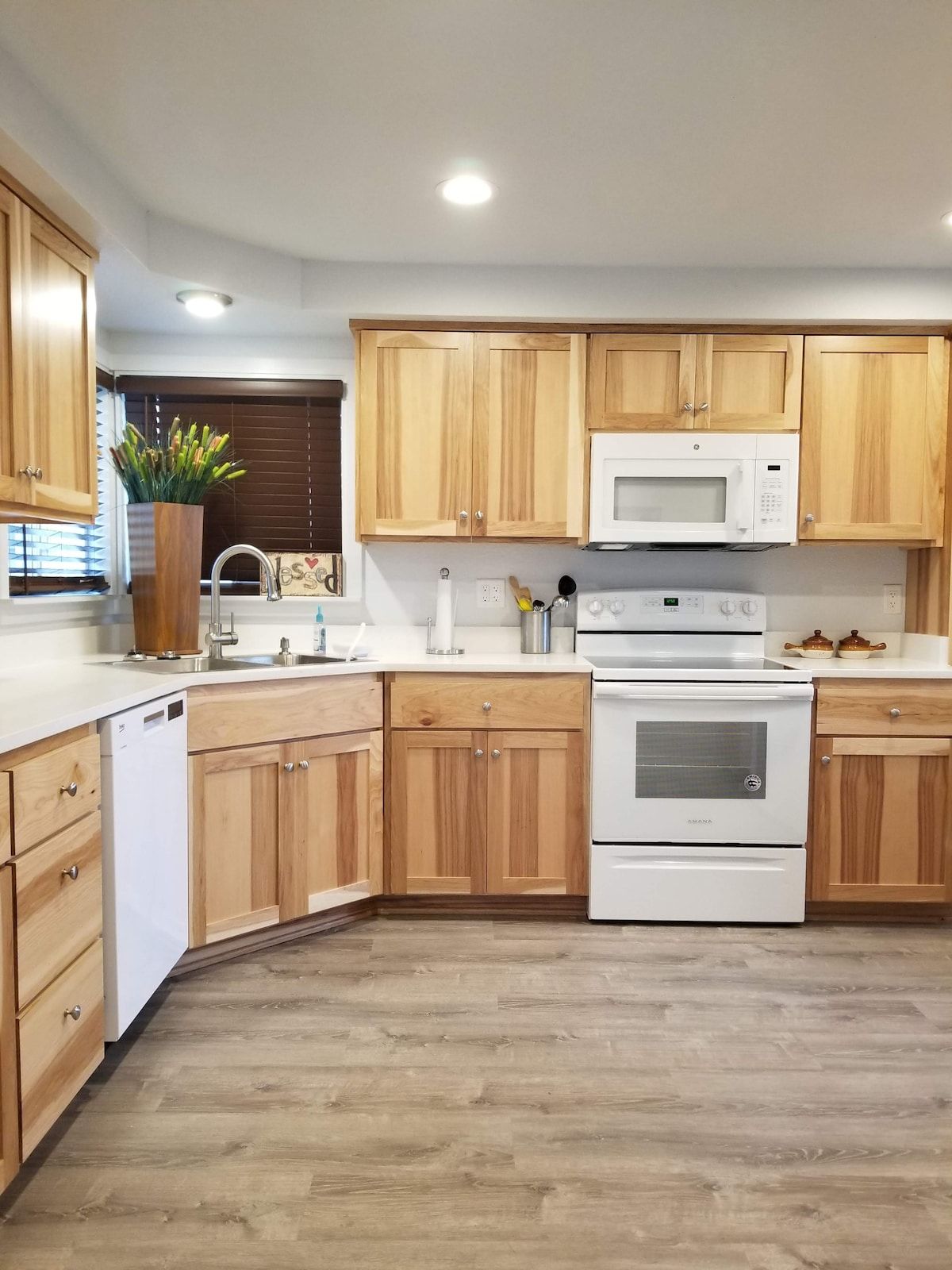 A modern kitchen with wooden cabinets, a white dishwasher, a microwave, and an oven.