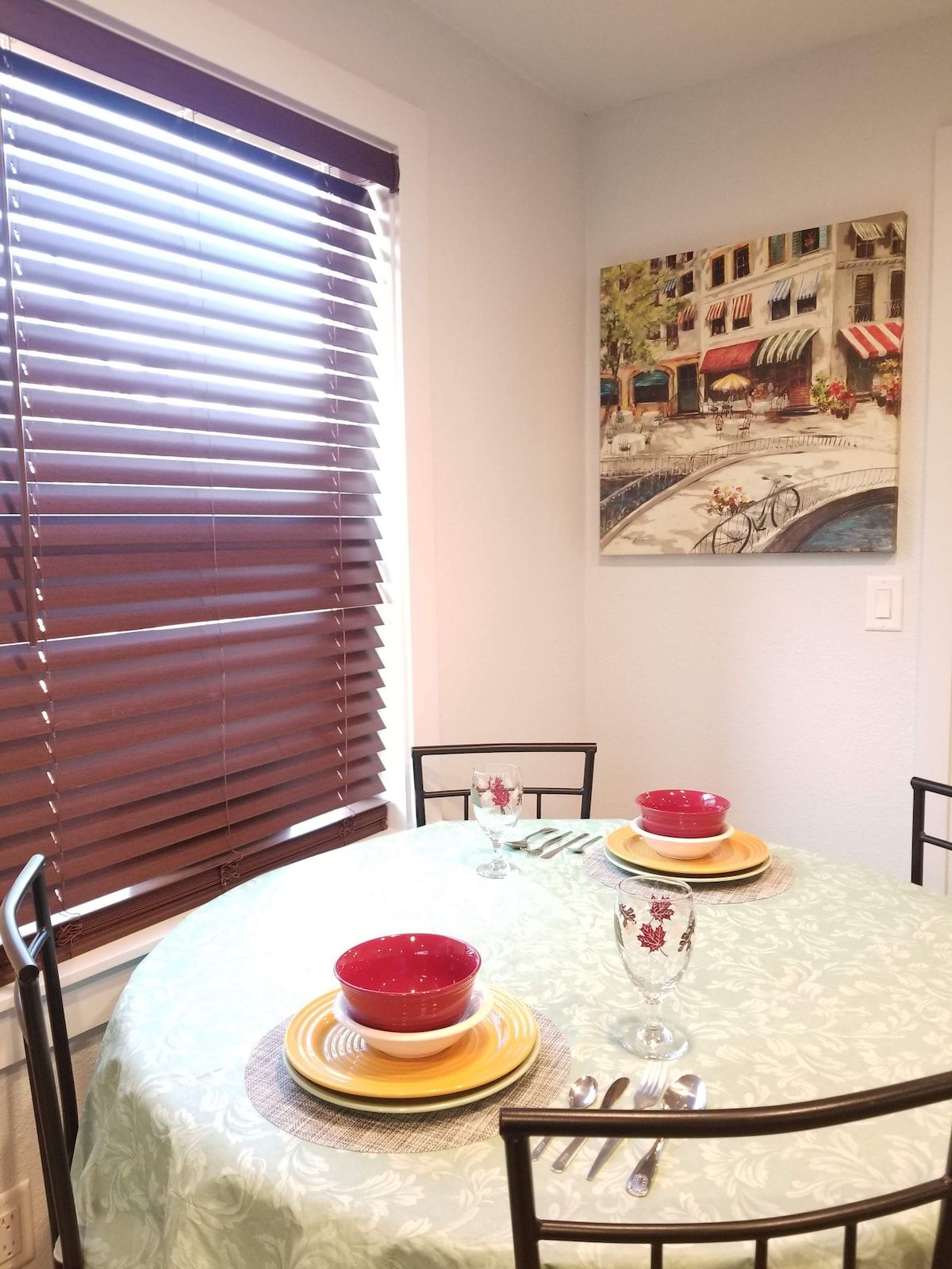 A dining table with a floral tablecloth, set with red bowls, plates, and cutlery.
