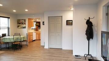A living room with a dining area, a kitchen in the background, and a coat rack with a jacket.
