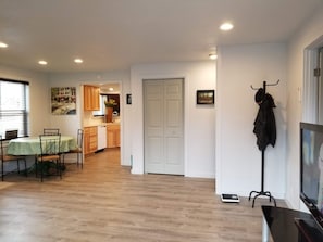 Ein Wohnzimmer mit Essbereich, eine Küche im Hintergrund und ein Kleiderhaken mit einem Jackett.