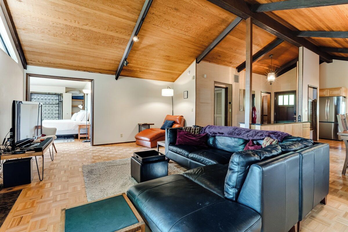 A spacious living area with a high ceiling, a leather sofa, a dining table, and a kitchen in the background.