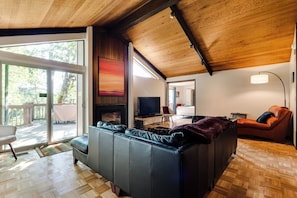 Ein modernes Wohnzimmer mit einer großen Eckcouch, einem Kamin, einem Fernseher und einem Essbereich, der durch eine Glastür einsehbar ist.