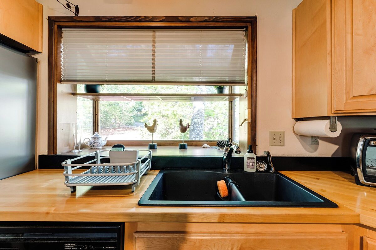 A kitchen with a sink, a window with blinds, a toaster, and a small shelf with kitchen items.