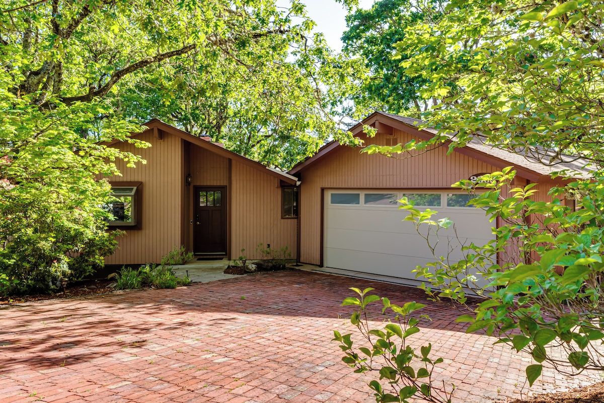 A two-story house with a garage, surrounded by trees and a brick driveway.