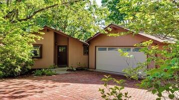 A two-story house with a garage, surrounded by trees and a brick driveway.
