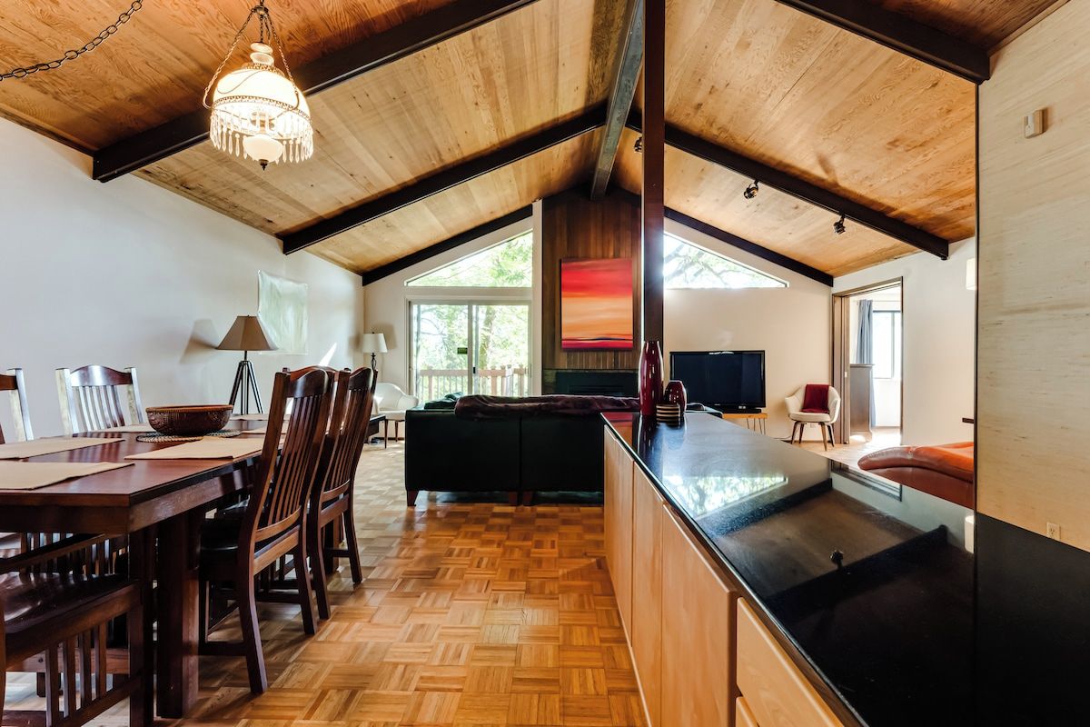 Une cuisine spacieuse avec un plafond en bois, un coin repas avec des chaises et une table, et une vue sur l’extérieur par une fenêtre.