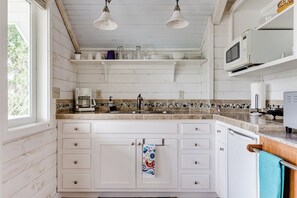 A kitchen with white cabinets, a tiled backsplash, and a window providing natural light. - Waterfront Studio Apartment w/ Balcony & Lake (Veneta)