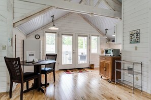 Ein geräumiges Zimmer mit Holzboden, einem Esstisch mit Stühlen, einer Küchenzeile mit Schränken und einer Mikrowelle sowie einem großen Fenster mit Blick ins Freie.