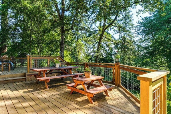 A wooden deck with picnic tables and a railing, surrounded by trees. - Scenic Eugene Home w/ Deck 1mi to UofO (Eugene)