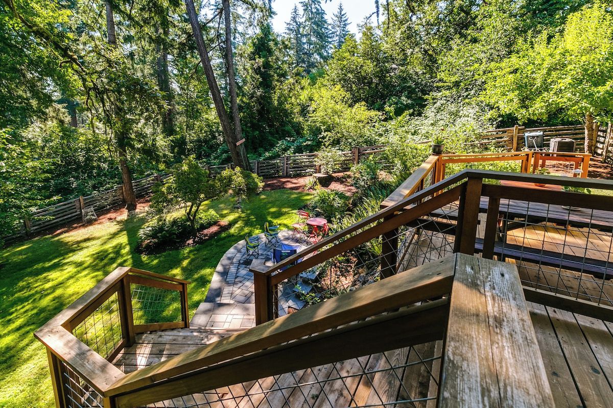 A wooden deck with a metal railing, surrounded by lush greenery and trees.