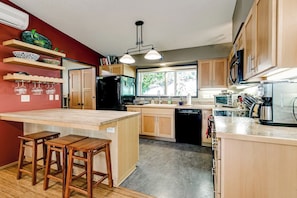 A kitchen with wooden cabinets, a central island with stools, a refrigerator, a microwave, and a window providing natural light. - Scenic Eugene Home w/ Deck 1mi to UofO (Eugene)