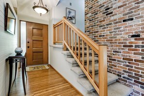 A staircase with wooden railings leading to a door, a small table with a vase, and a brick wall. - Scenic Eugene Home w/ Deck 1mi to UofO (Eugene)
