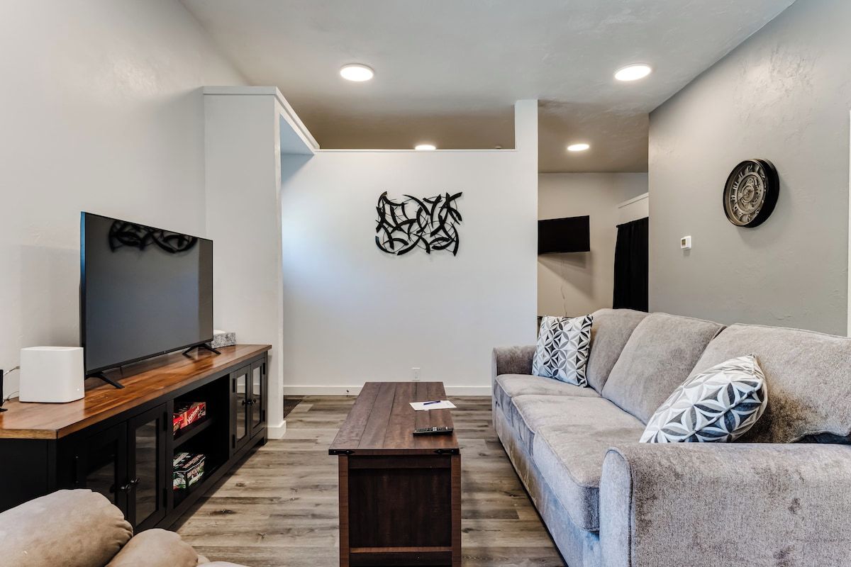 A modern living room with a flat-screen TV, a wooden coffee table, and a grey sofa with patterned cushions.