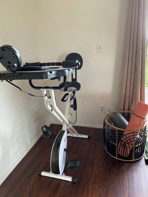 Ein stehendes Fitnessrad mit Gewichtescheibe und einem Korb mit aufgerollten Matten.
