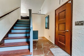 Eine Treppe mit Holzdielen führt zu einer Empore, eine Holztür mit einer Hausnummer und ein Steinfußboden.