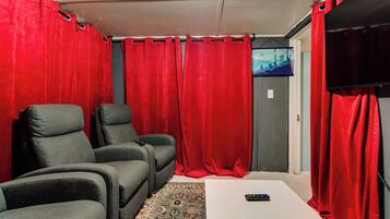 A room with two grey armchairs, a white table, and red curtains.