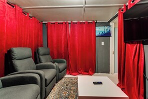 Ein Zimmer mit zwei grauen Sesseln, einem weißen Tisch und roten Vorhängen.