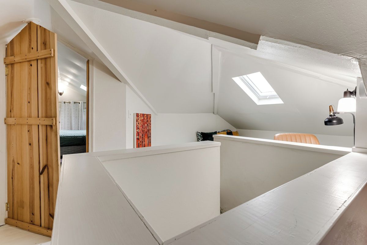 A modern loft bedroom with a sloped ceiling, skylight, and a wooden door.
