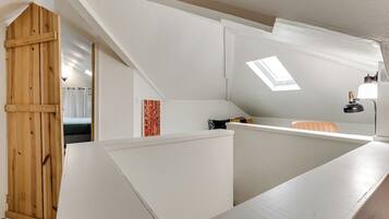 A modern loft bedroom with a sloped ceiling, skylight, and a wooden door.