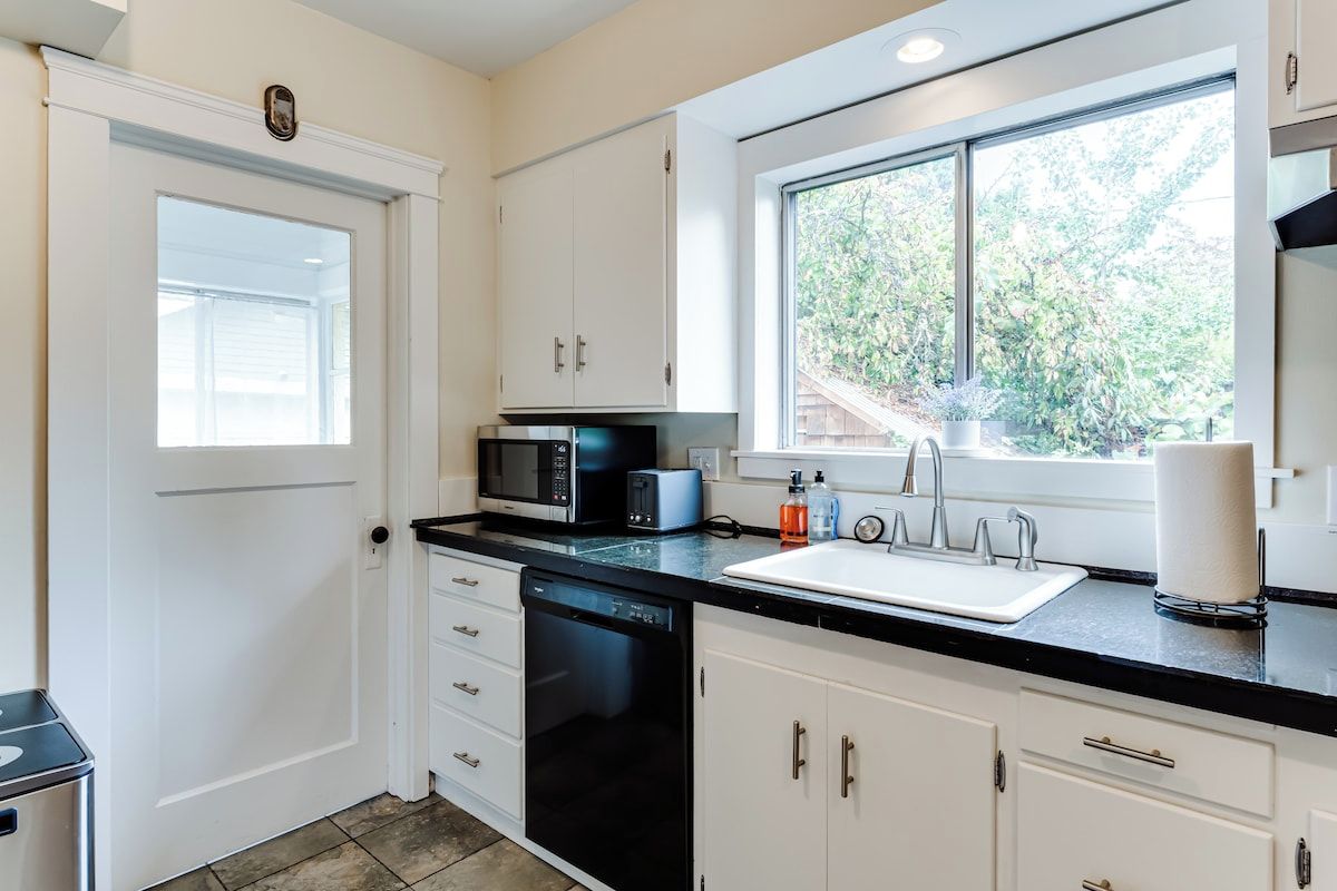 A kitchen with white cabinets, a black dishwasher, a microwave, and a sink.