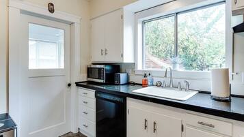 A kitchen with white cabinets, a black dishwasher, a microwave, and a sink.