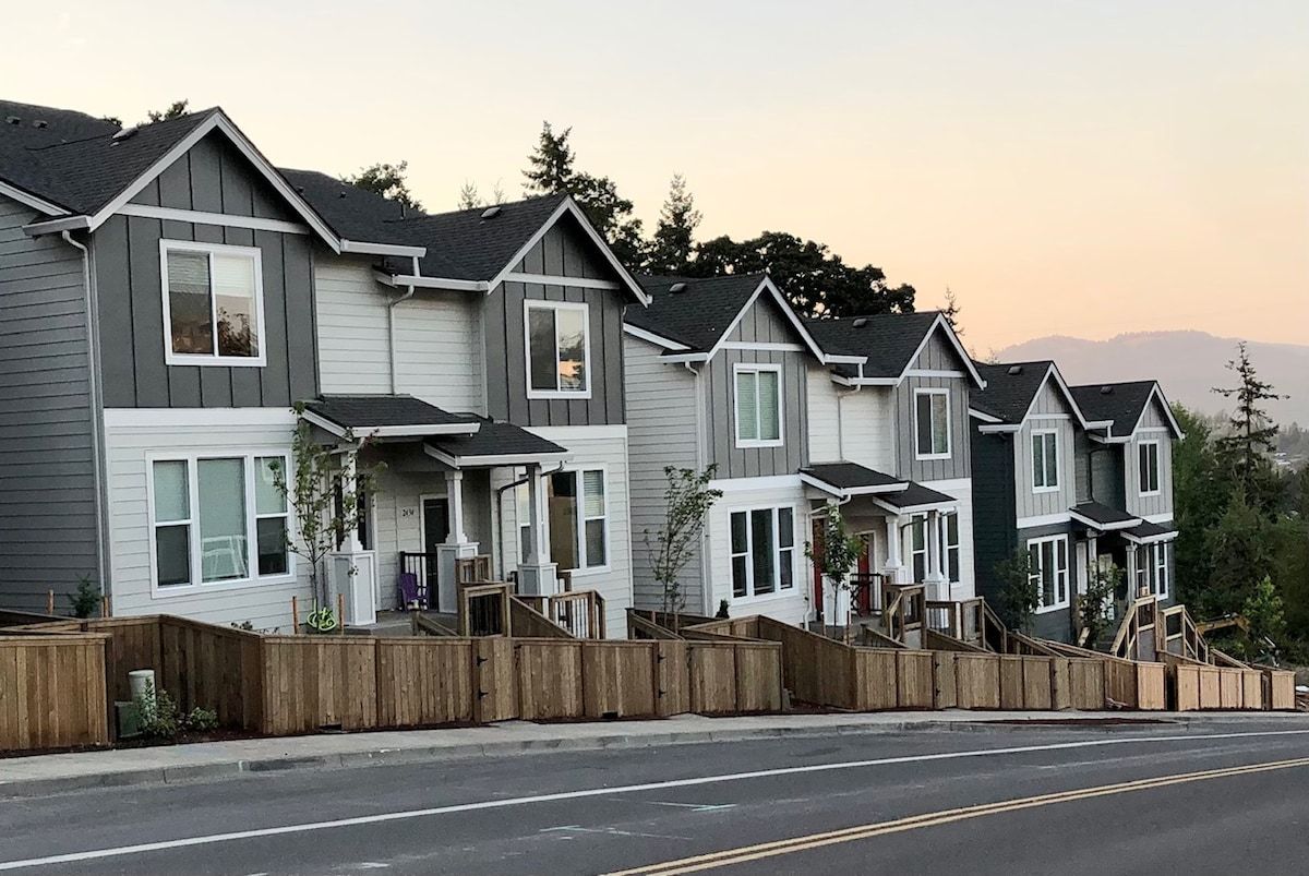 Une rangée de maisons de ville avec des porches à l’avant, des clôtures en bois et une rue au premier plan.