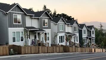 Une rangée de maisons de ville avec des porches à l’avant, des clôtures en bois et une rue au premier plan.