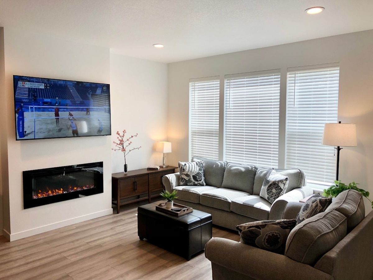 Una sala de estar moderna con un televisor de pantalla plana montado en la pared, una chimenea, un conjunto de sofás, una mesa de centro y una lámpara de pie.