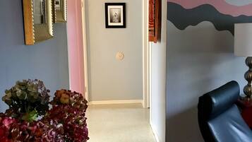 Un pasillo con una puerta, un cuadro en la pared, un jarrón con flores y una silla.