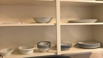 Ett kök med vita hyllor, en svart mikrovågsugn och olika skålar och tallrikar.