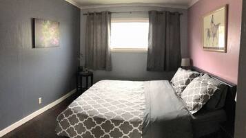 A bedroom with a bed, curtains, a window, a nightstand, and a wall-mounted picture.
