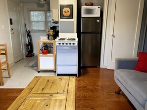A compact kitchen with a stove, oven, and refrigerator, a wooden table, and a grey sofa. - Comfortable Apartment in a Convenient location. (Springfield)