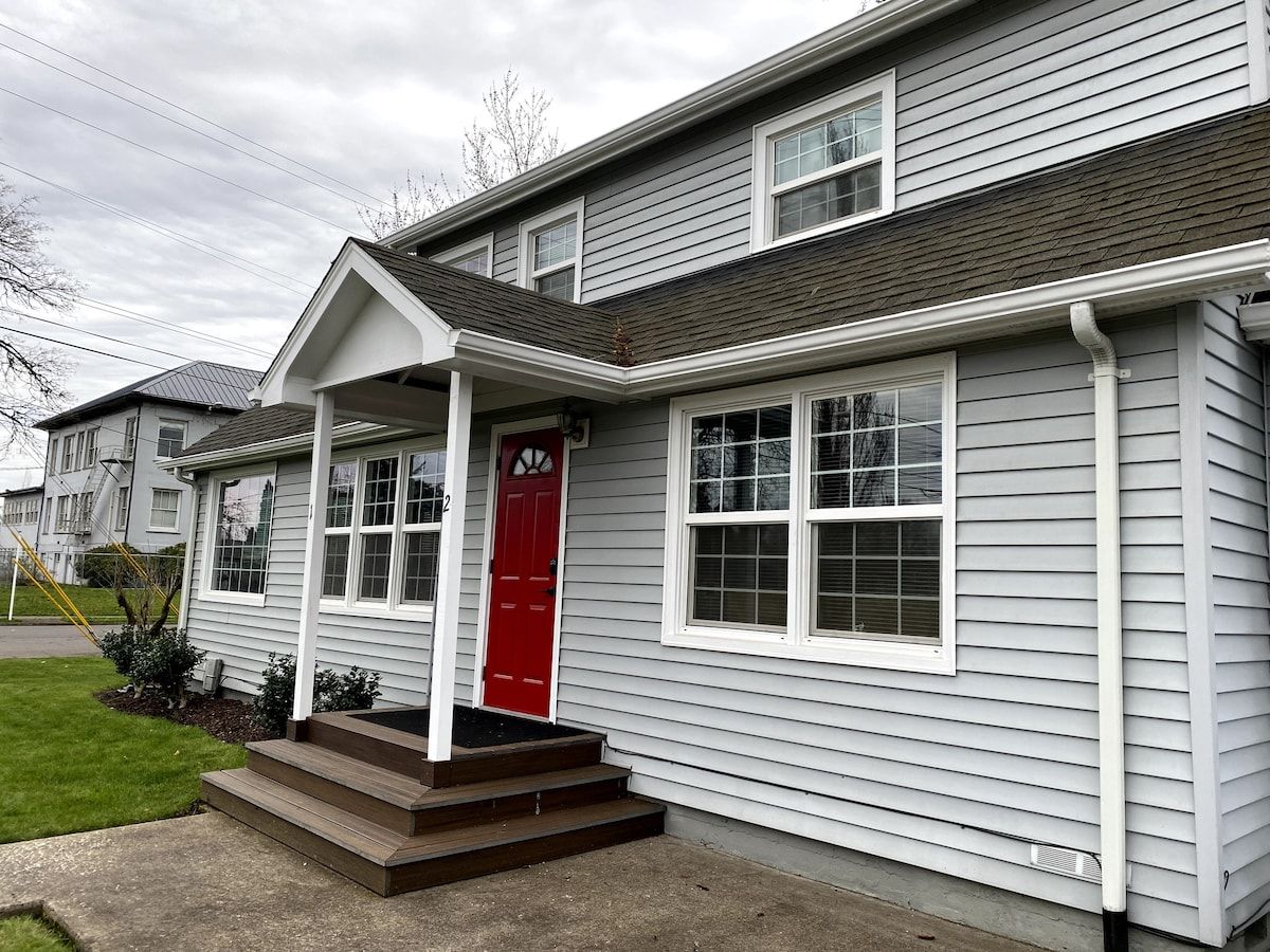 A two-story residential building with a red door, white windows, and a covered porch.