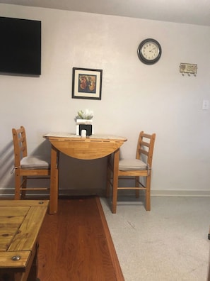 A dining area with a wooden table and two chairs, a clock on the wall, and a framed picture above the table. - Comfortable Apartment in a Convenient location. (Springfield)
