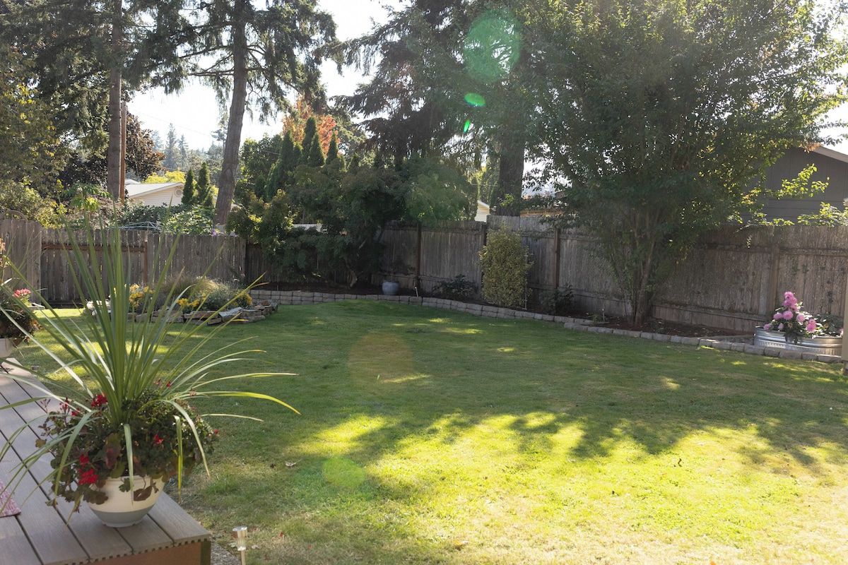 Un jardin avec une clôture en bois, une pelouse et un pot de fleurs.