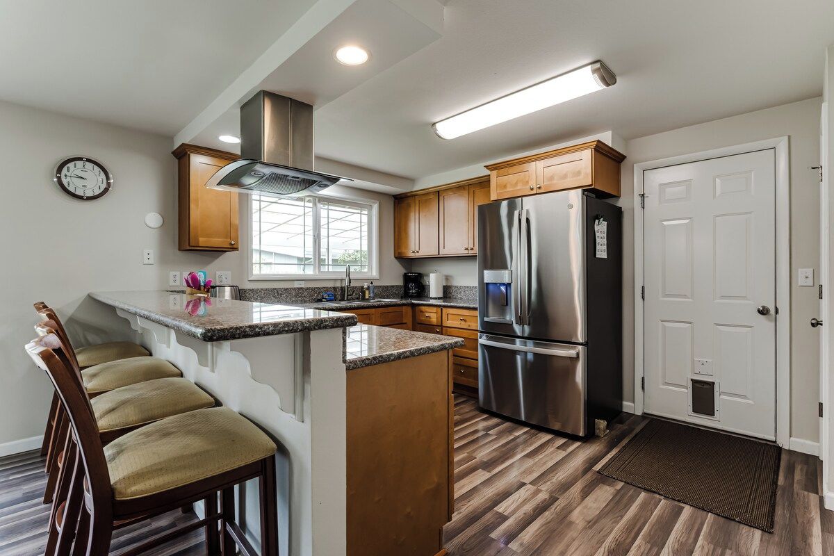 A modern kitchen with a central island, stainless steel appliances, wooden cabinets, and a built-in clock.