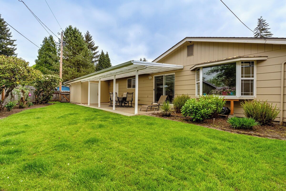 A single-story house with a covered patio, a lawn, and a small garden.