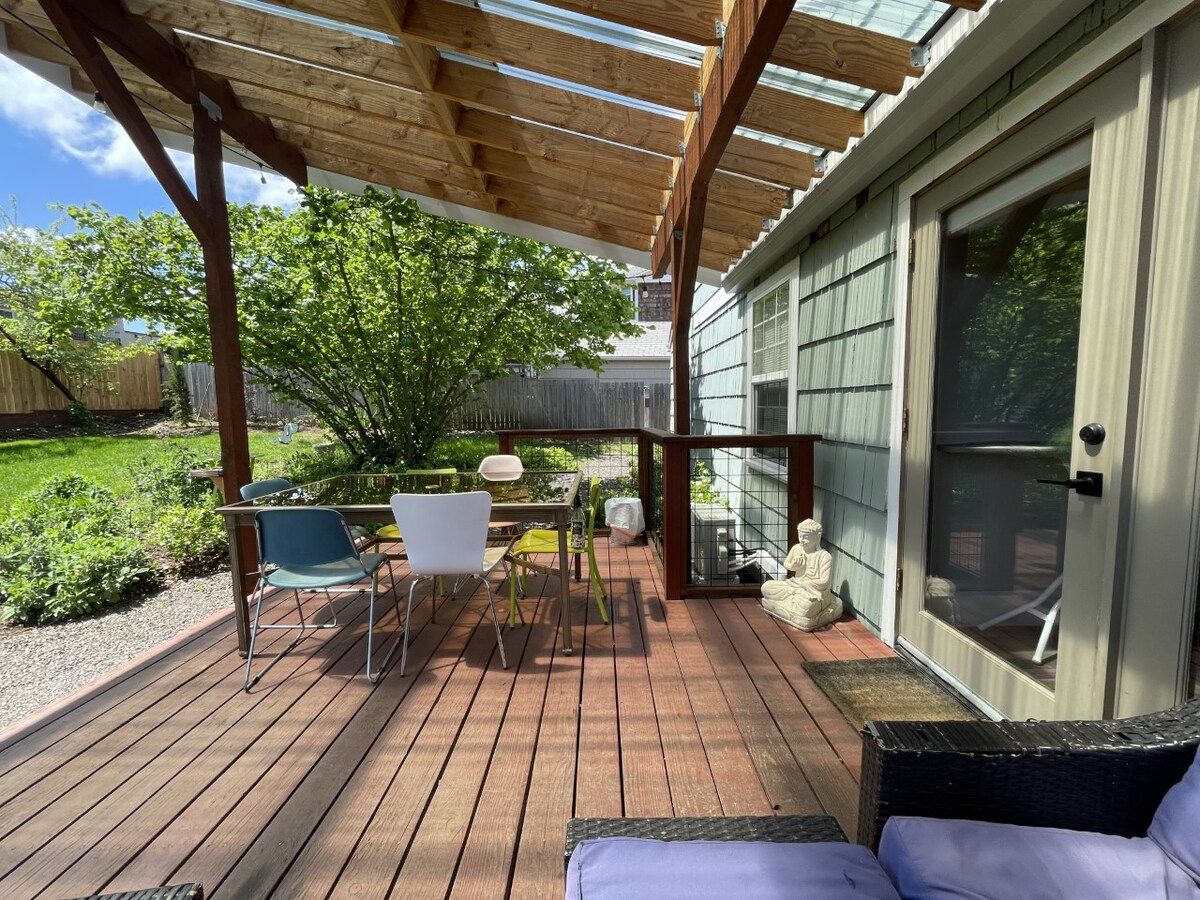 Een houten terras met buitenmeubilair, een pergola en een huis met een schuifdeur van glas.