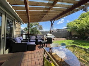 An outdoor patio with a covered seating area, a grill, and a glass table. - City-Center Home w/ Fenced Yard, Walk to Shopping (Eugene)