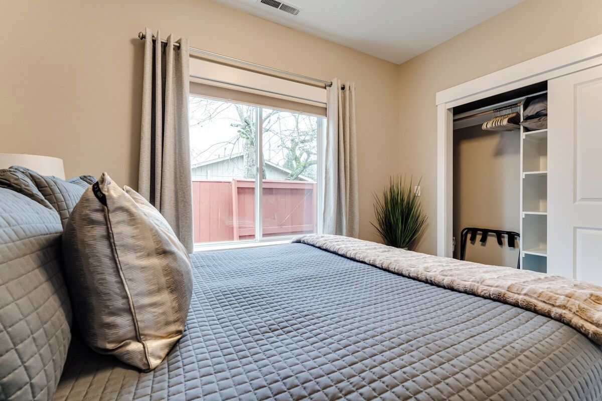 A bedroom with a bed, a window with curtains, a closet, and a plant.