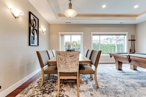 A dining area with a pool table, a dining table with chairs, and a view of the outdoors through large windows. - Luxury Pool Table House Near UO & Airport (Eugene)