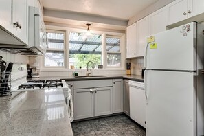A kitchen with white cabinets, a gas stove, a refrigerator, and a window with a view of greenery. - Central Home, Covered Deck Near Whiteaker District (Eugene)