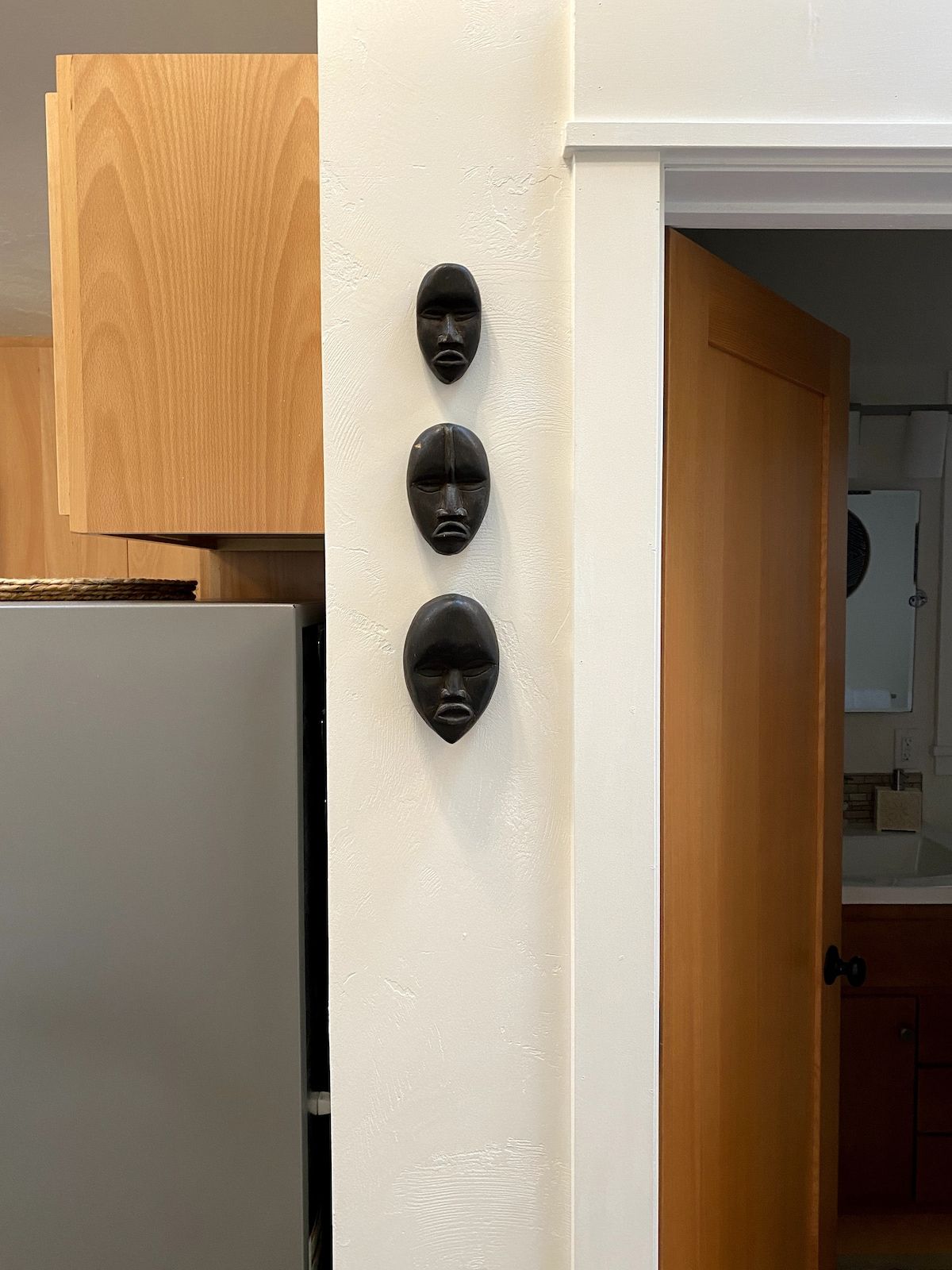 A kitchen with a white refrigerator, wooden cabinets, and a white wall with three black decorative objects.